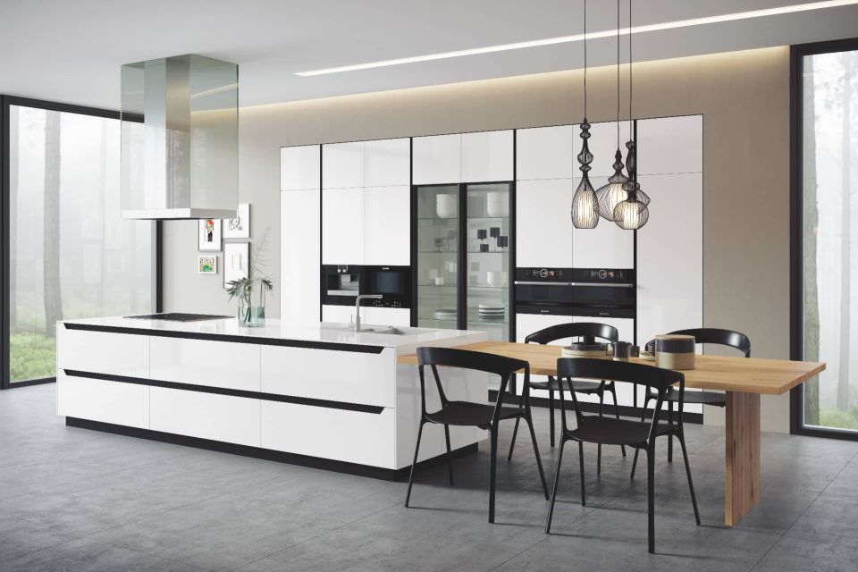 Cocina a medida con puertas blancas, gola negra, vitrinas y mesa de comedor integrada.