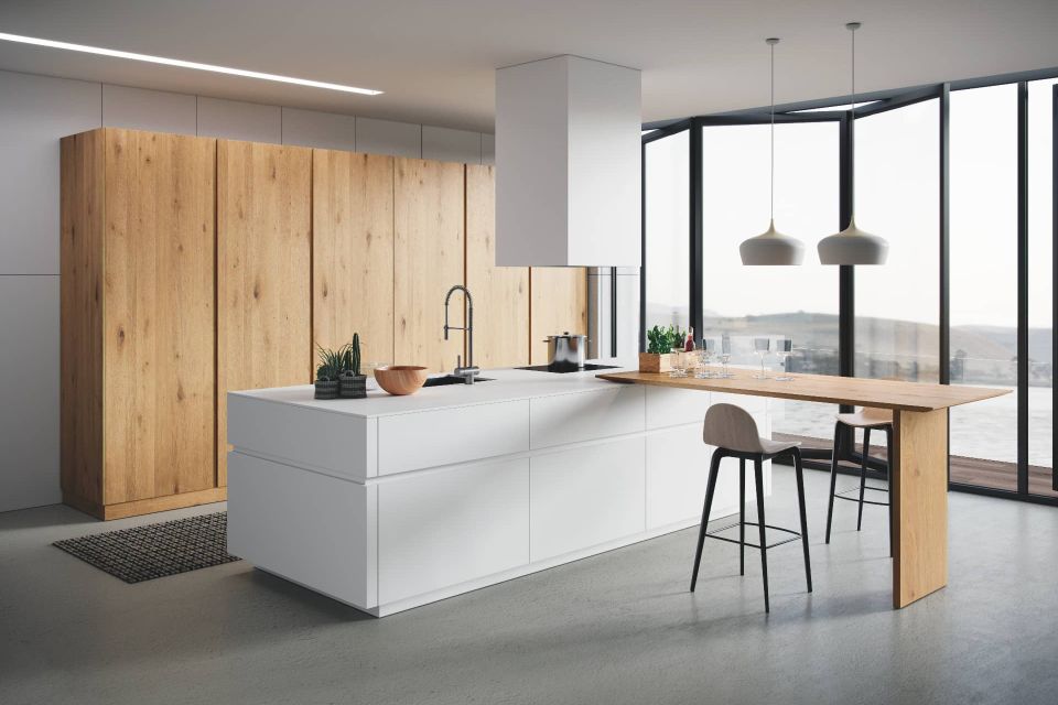 Cocina a medida con gabinetes de madera clara, isla blanca mate.