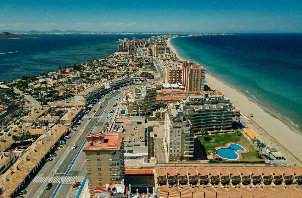Vista aérea de La Manga del Mar Menor en Murcia, España, mostrando desarrollo residencial, playas de arena y aguas turquesas del Mar Menor y Mediterráneo.