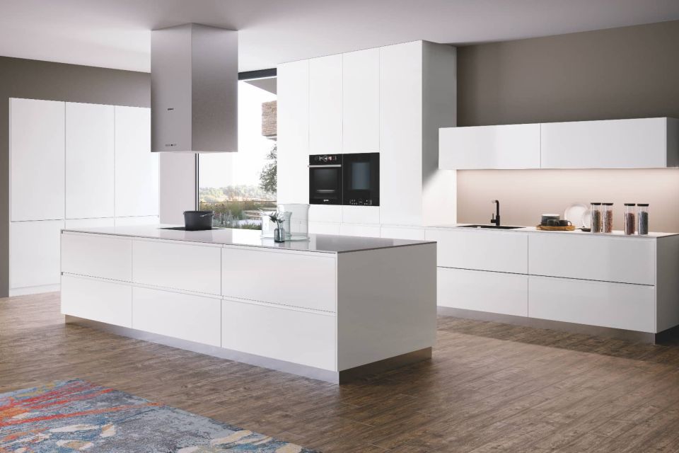 Cocina a medida con gabinetes blanco brillo, isla central y equipamiento integrado negro.